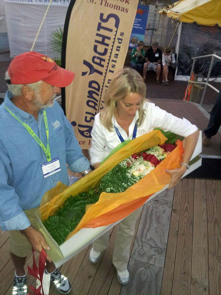 A man and a woman are holding a box of flowers in front of a sign that says island yachts