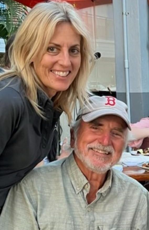 A woman is standing next to a man wearing a hat with the letter b on it.