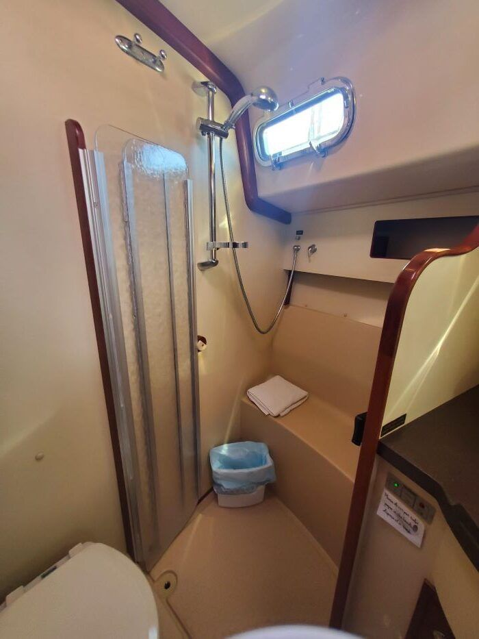 A bathroom on a boat with a toilet , shower and window.