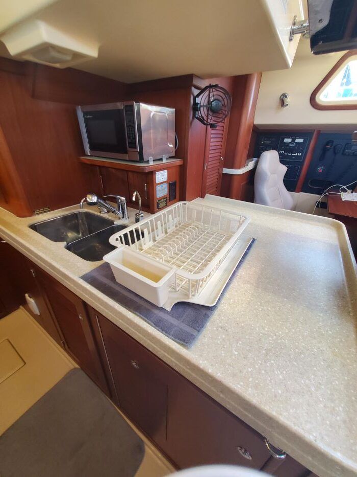 A kitchen on a boat with a sink , microwave , and drying rack.