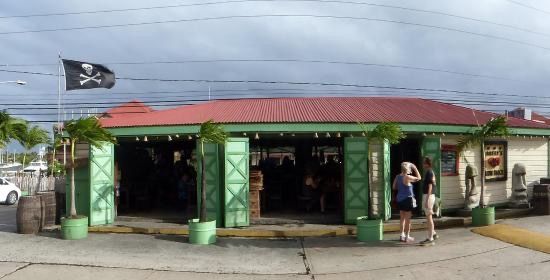 A row of open-air stalls with bright clothing and umbrellas, set against a backdrop of a lush green hillside.