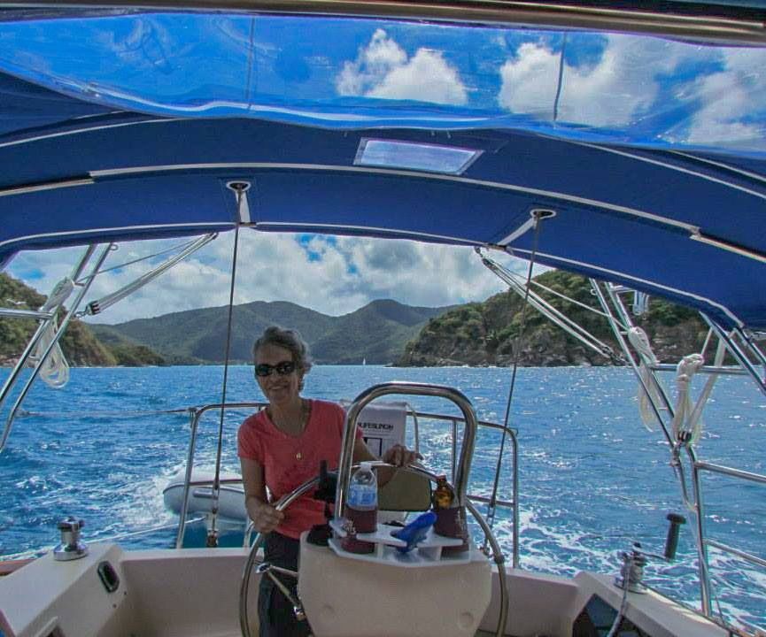 A woman is sitting at the helm of a sailboat in the ocean.