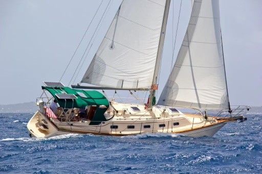 Sailboat on blue water with sails up; tan hull, green awning, American flag.
