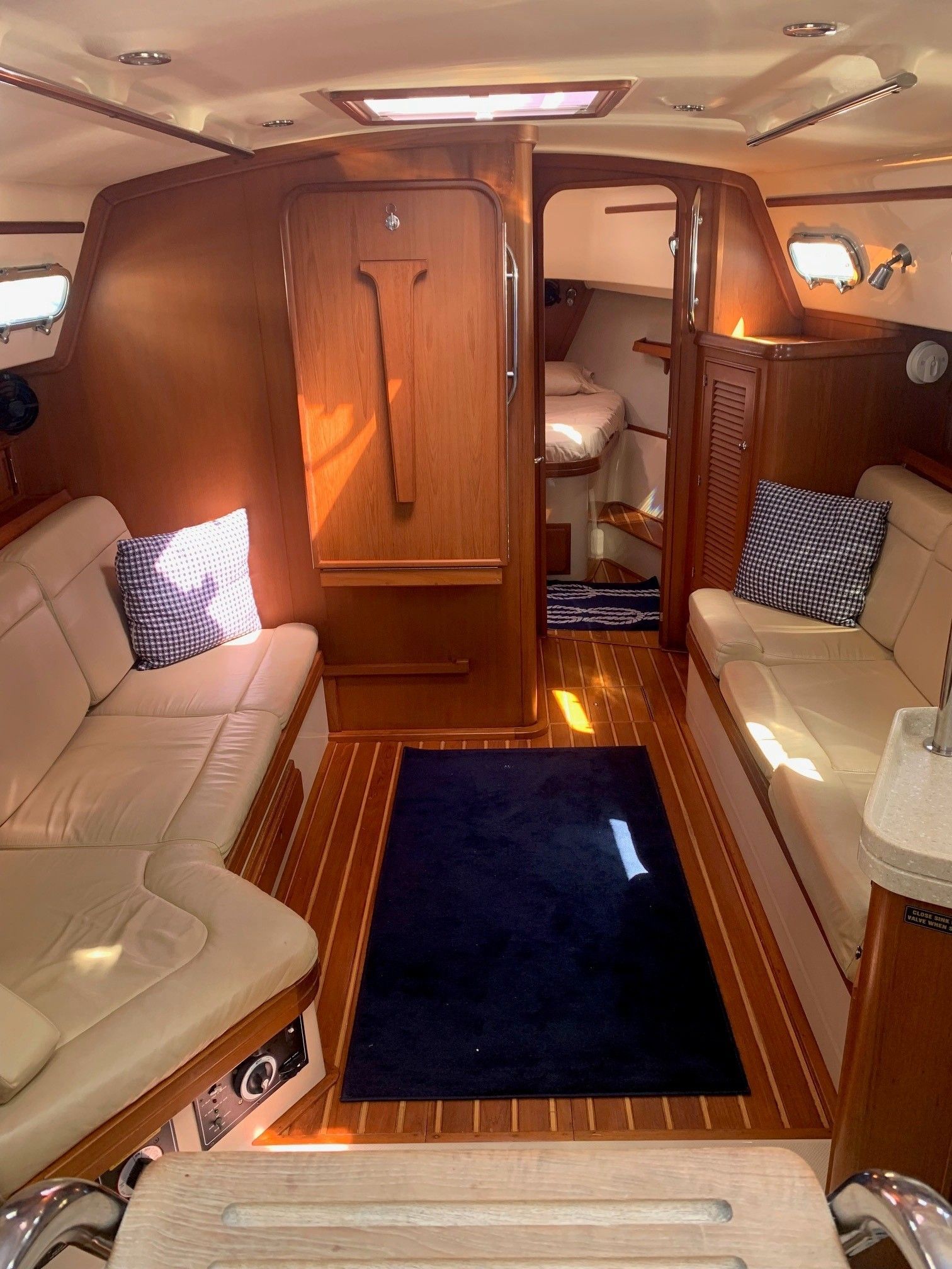 Interior of a yacht with wooden paneling, cream-colored couches, and a navy rug; a cabin entrance visible.