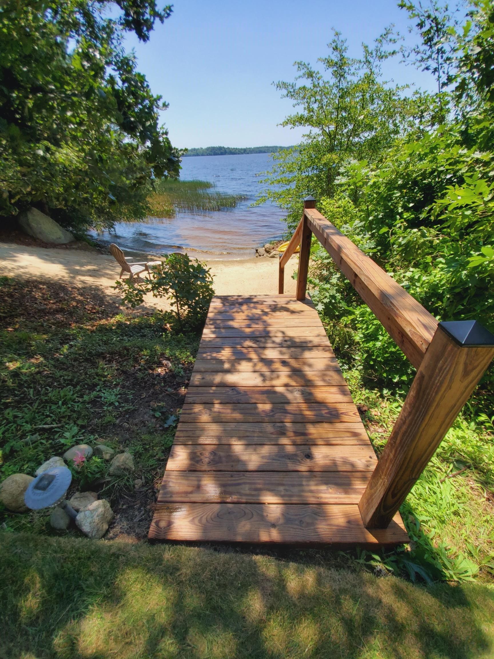 Wooden walkway with railing leads to sandy beach and lake.