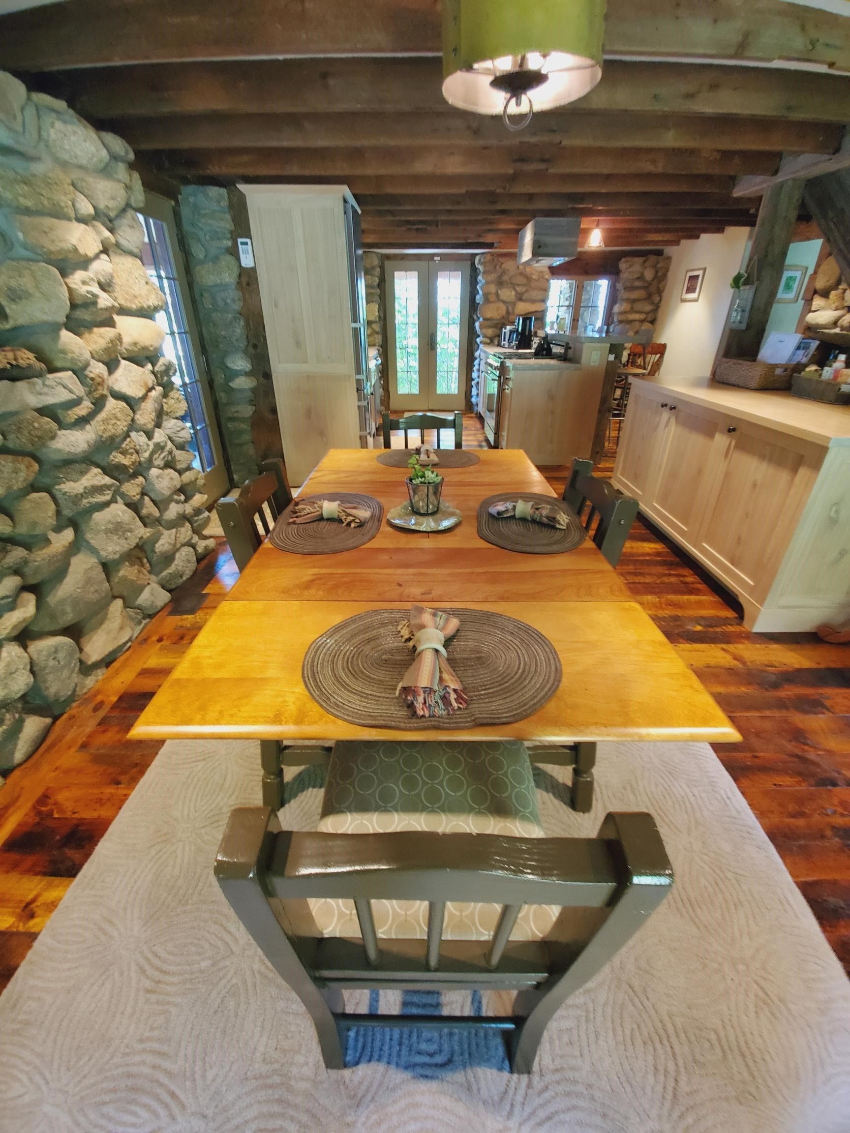 Dining room with stone wall, wooden table, and cabinets; rug on wooden floor.