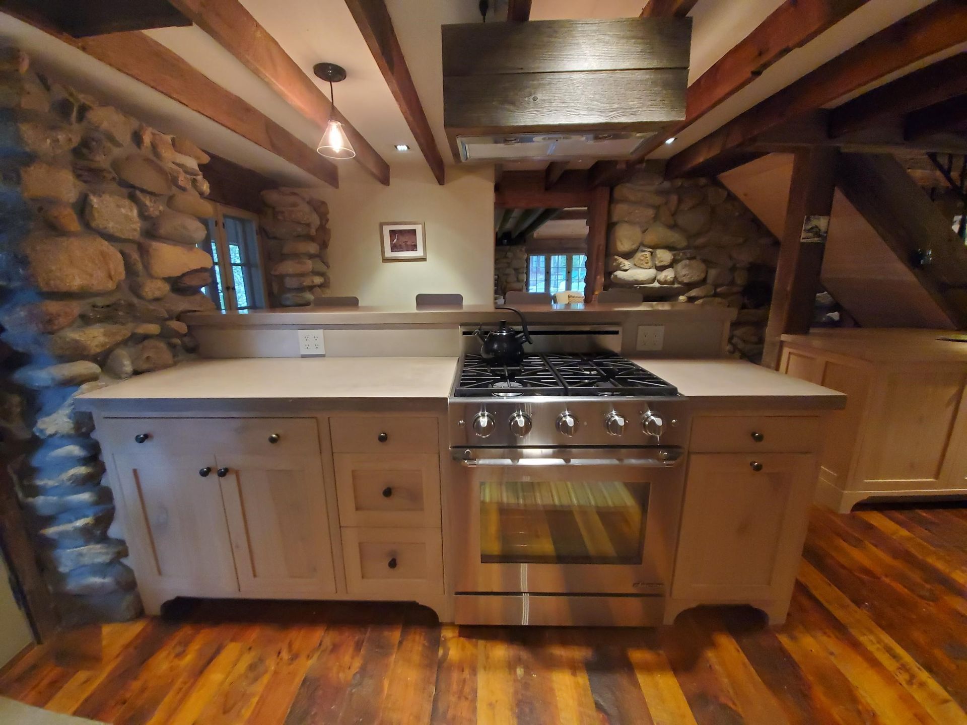 Kitchen with stone walls, light cabinets, stainless steel range, and wood beams.