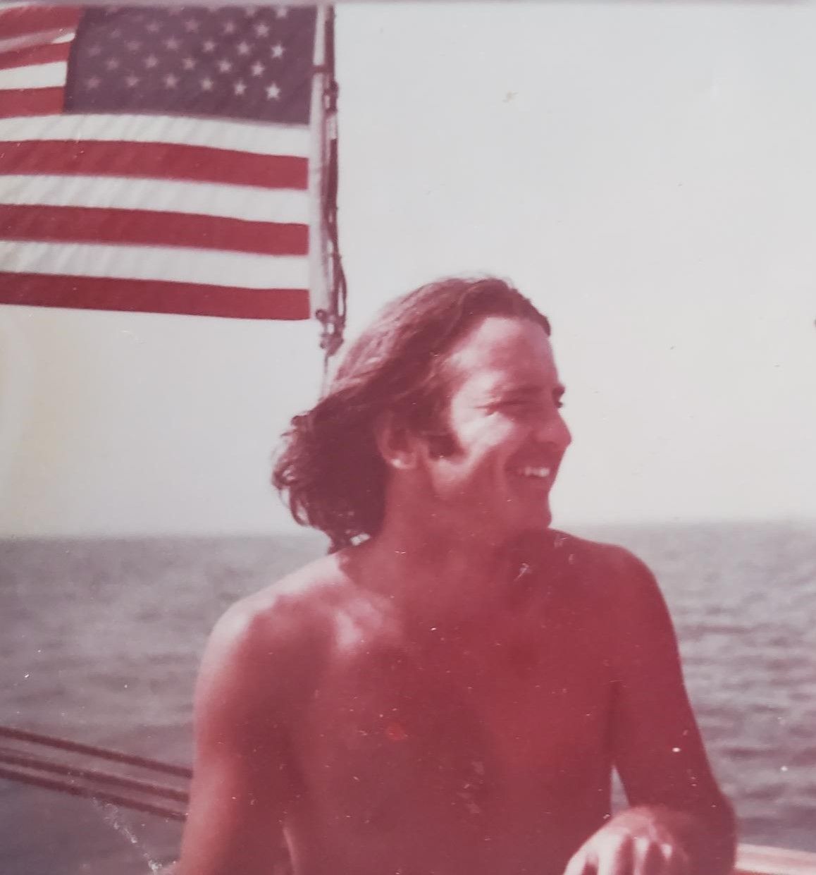 A shirtless man is smiling in front of an american flag