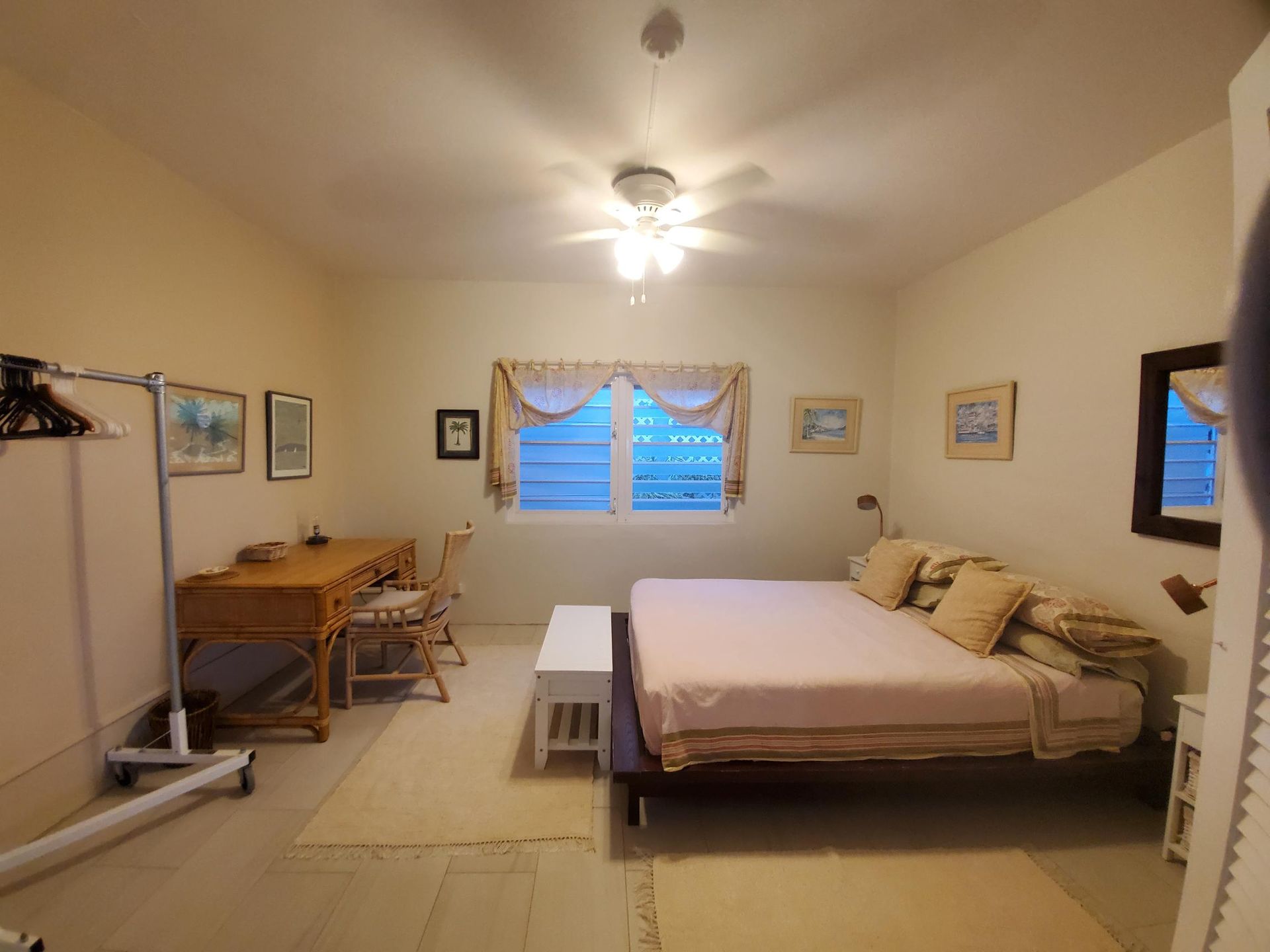 Bedroom with bed, desk, artwork, window, and a clothes rack.