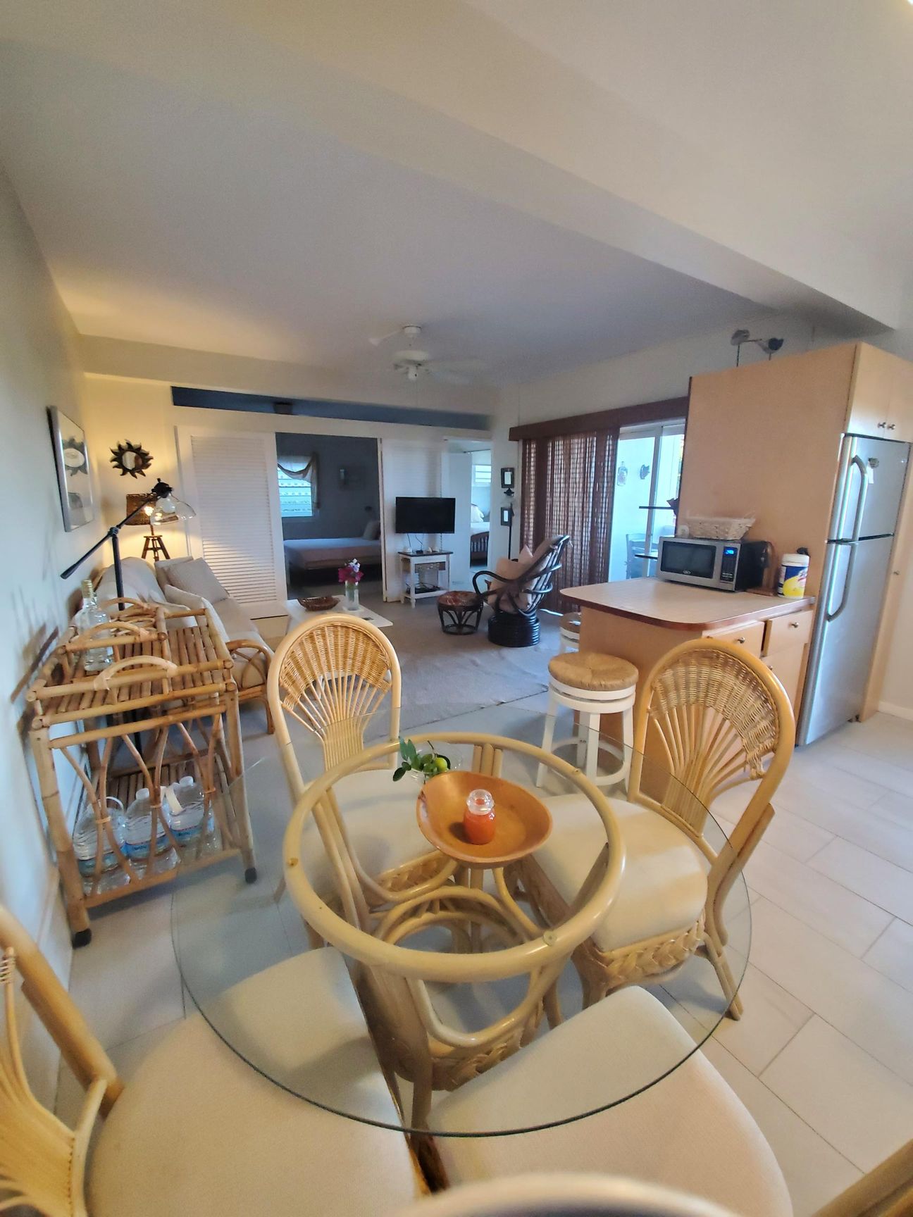 Dining area with wicker table and chairs, adjacent to a kitchen with a stainless steel refrigerator.