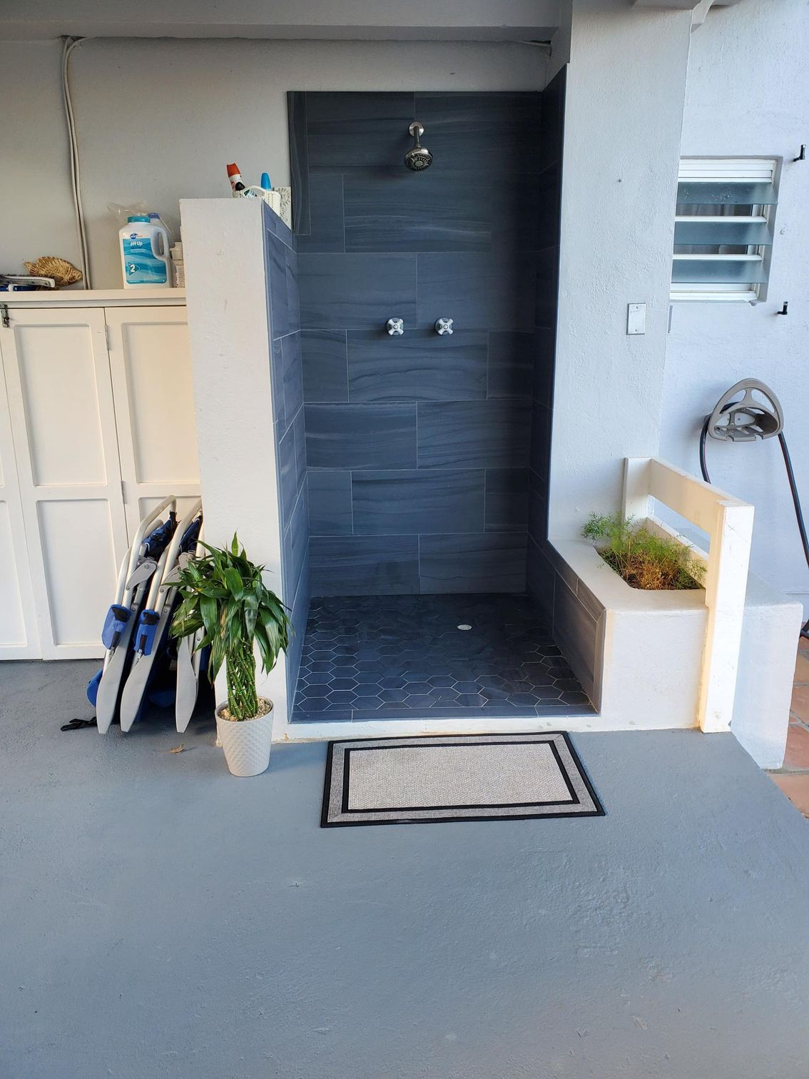 Outdoor shower with dark tiled walls, white border, and gray floor.