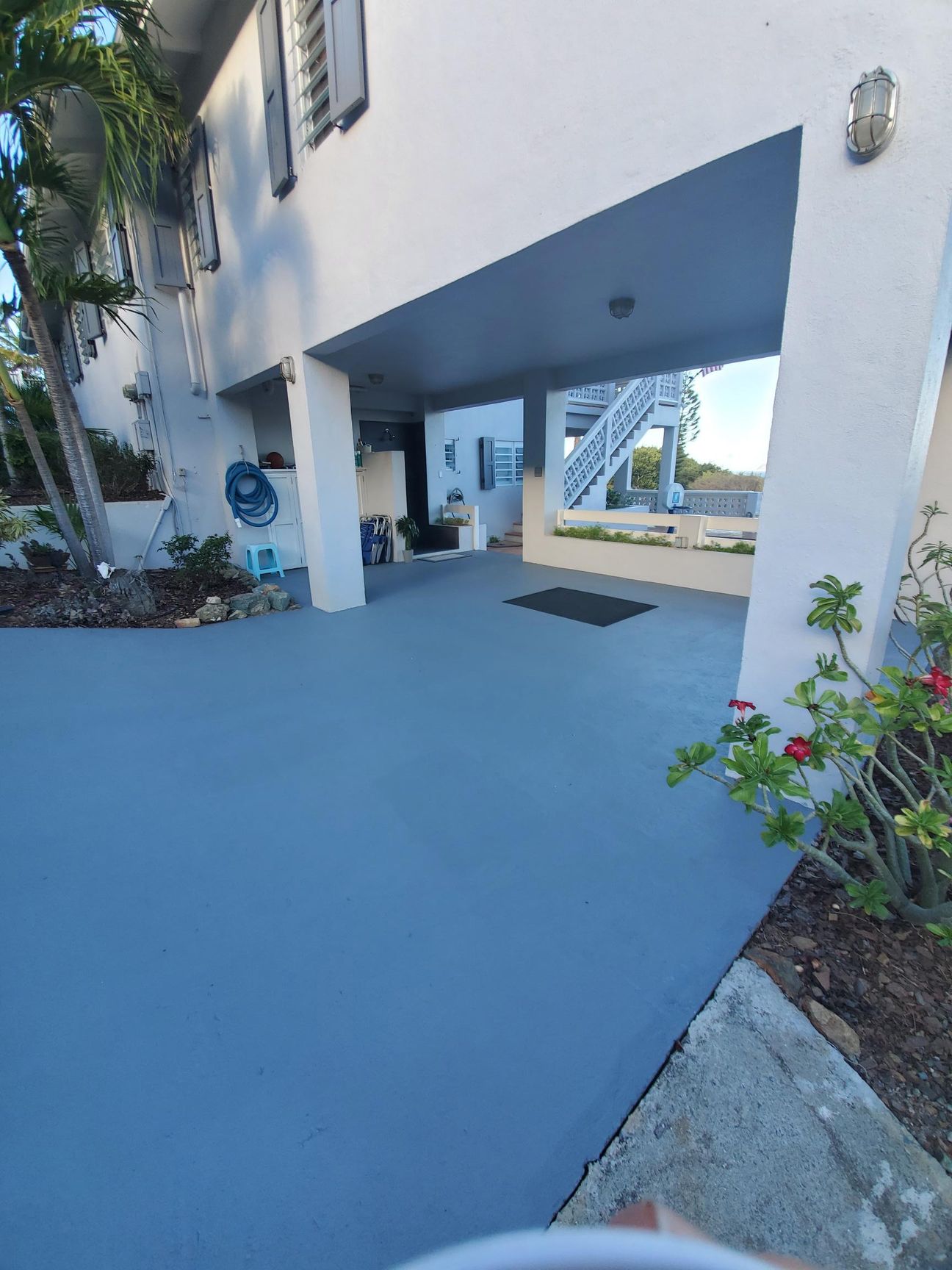 Blue painted carport with white building, palm tree, and stairs.