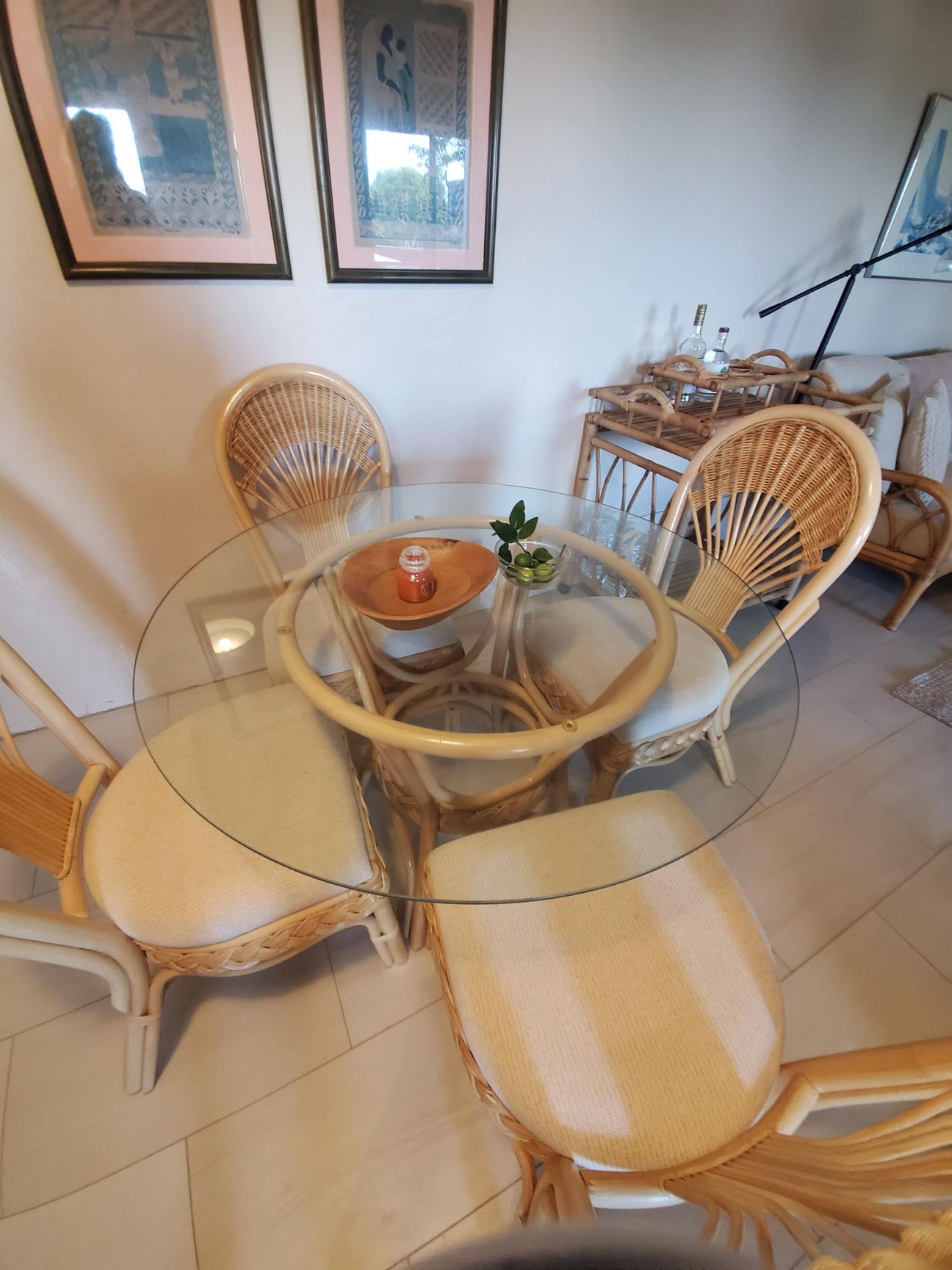 Round glass dining table with four woven chairs. Decorative items on table and wall.