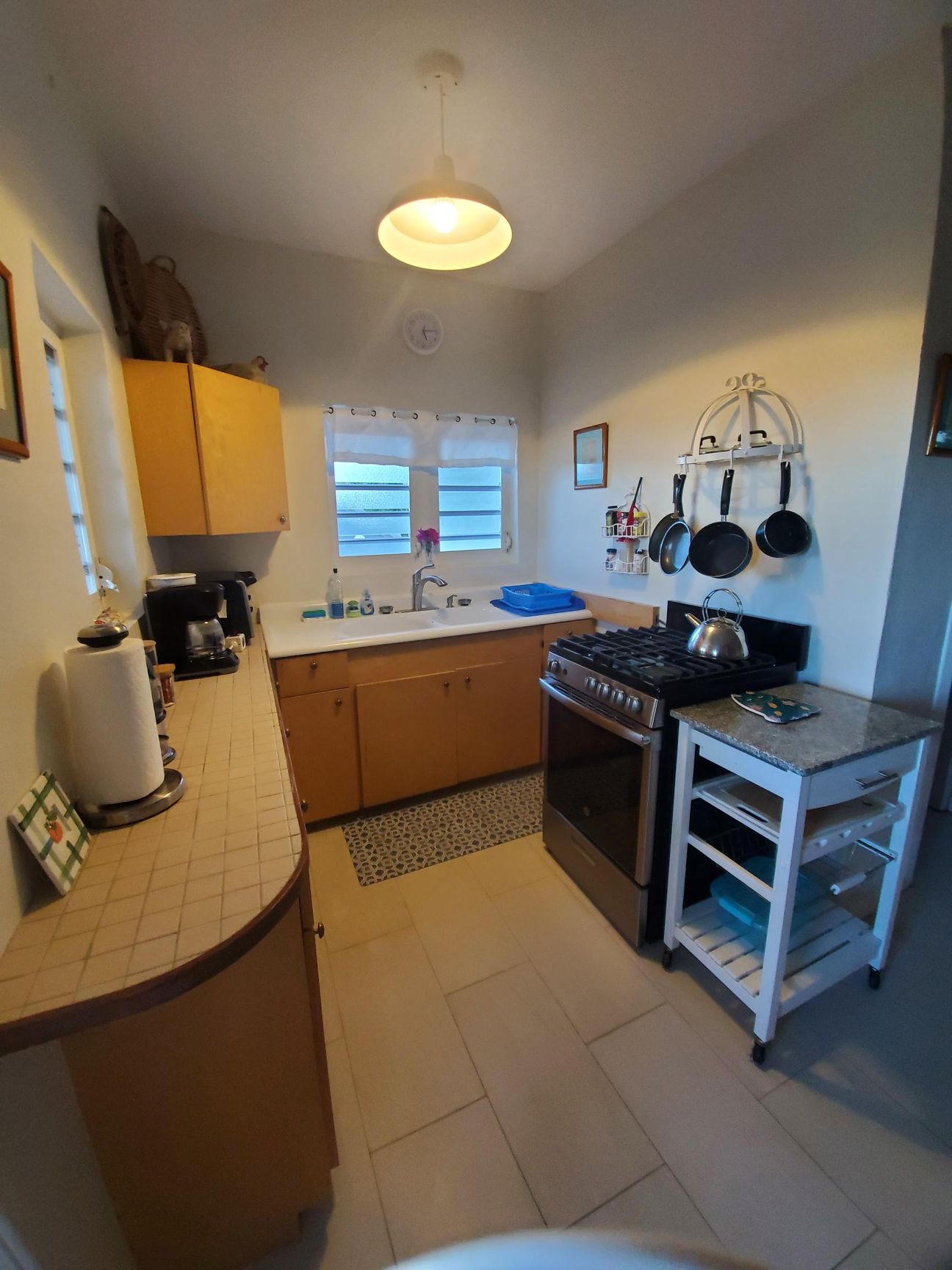 Kitchen with light wood cabinets, stainless steel stove, and white tile floor.