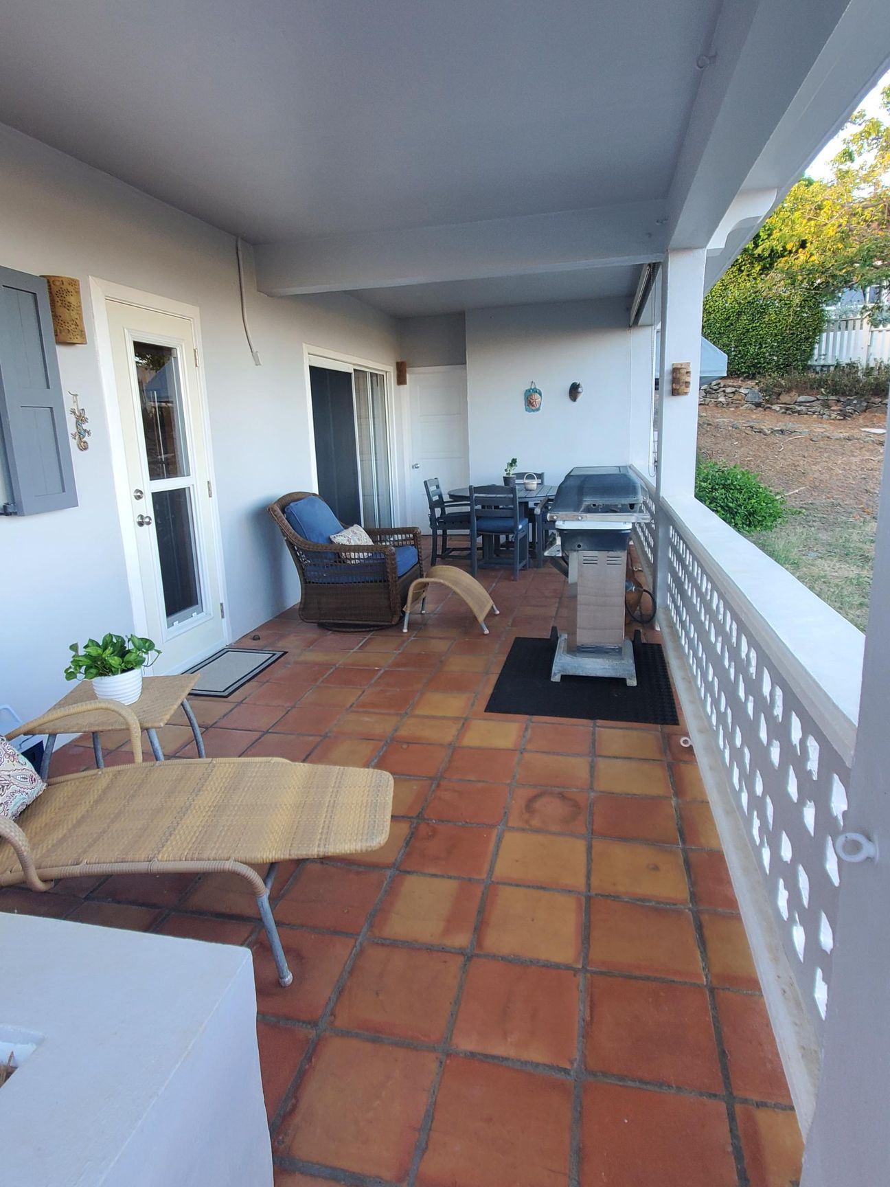 Patio with terracotta tile flooring, seating, grill, and view of trees.