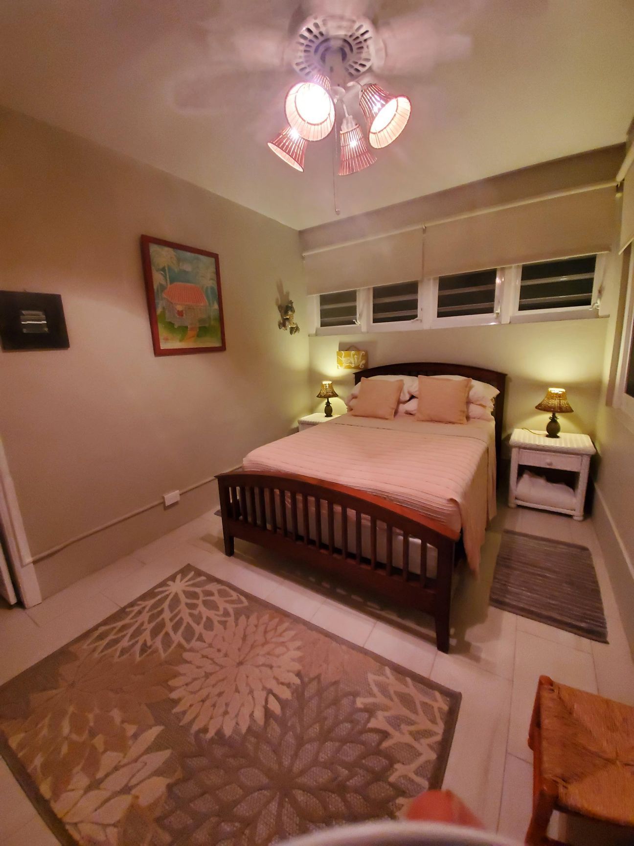 Bedroom with bed, nightstands, rug, artwork, and ceiling fan with pink lampshades.