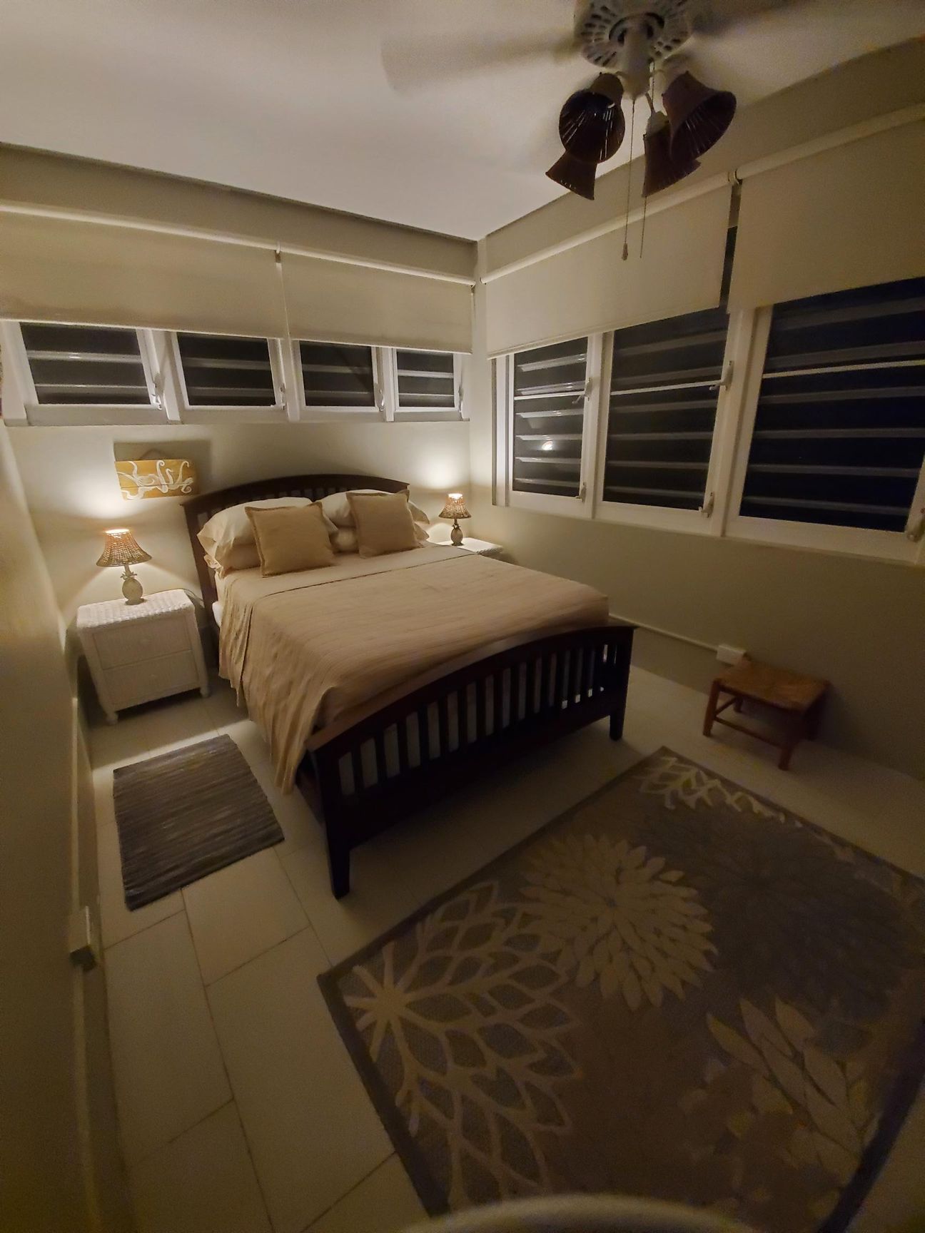 Bedroom with a dark wooden bed, two lamps, windows with blinds, and two rugs.