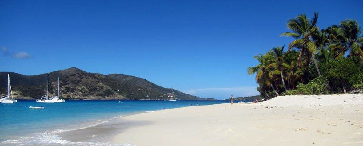 A beach with boats in the water and mountains in the background.