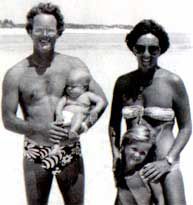 A man and a woman are standing next to each other on the beach holding a baby.