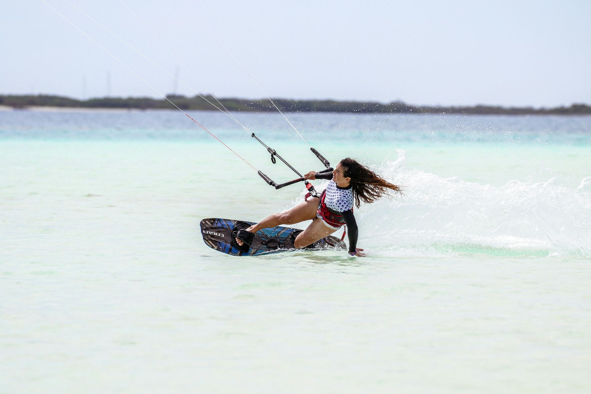 Woman kitesurfing on a board, turquoise water, kite overhead, spray, sunny day.