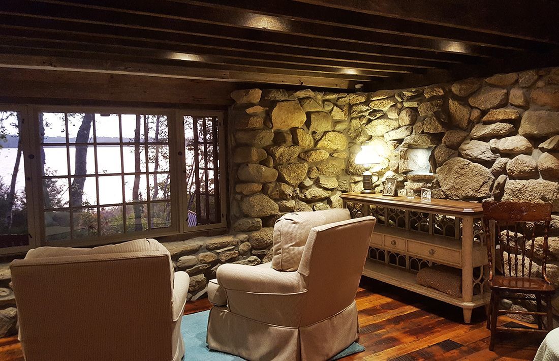 A living room with a stone wall , two chairs , a table and a window.
