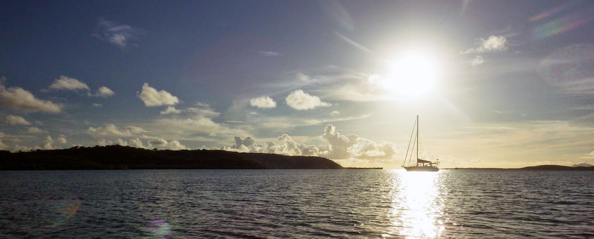 A sailboat is floating on top of a body of water at sunset.