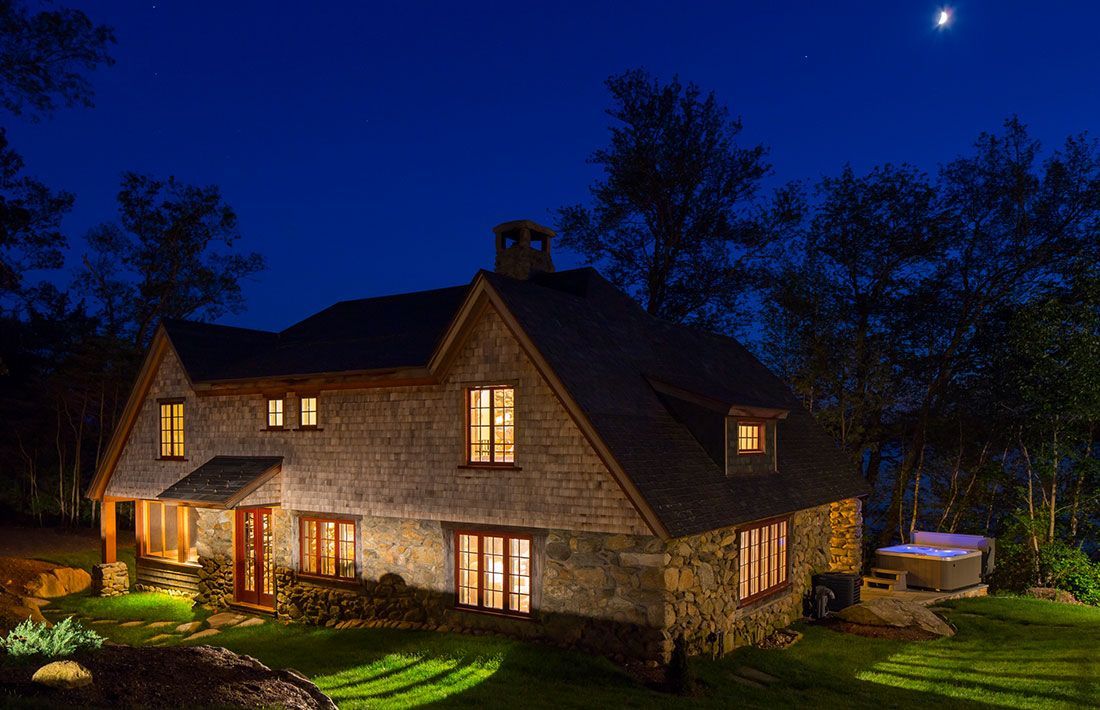 A large stone house is lit up at night with a hot tub in the backyard.