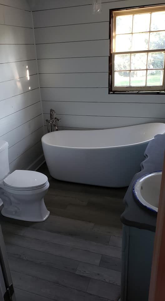 A bathroom with a toilet , bathtub , sink and window.