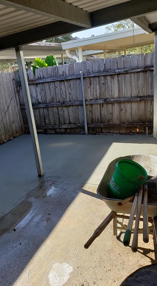A wheelbarrow is sitting under a covered patio next to a wooden fence.