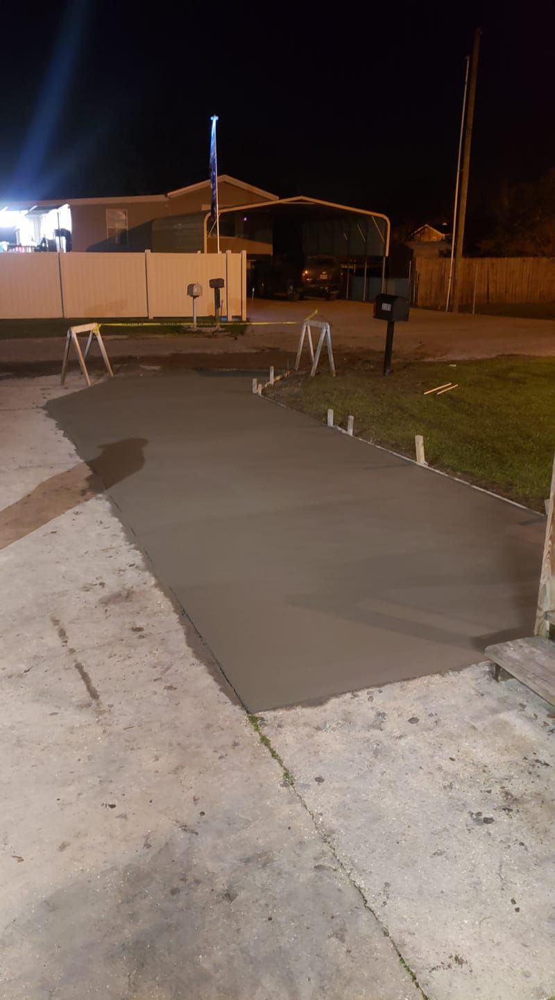 A concrete driveway is being built at night in front of a house.