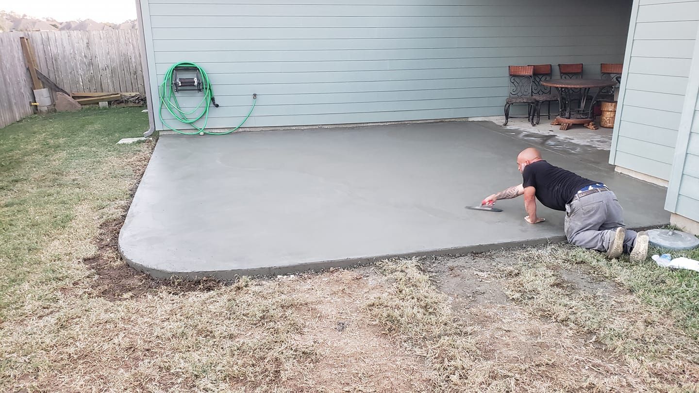 A man is kneeling on the ground working on a concrete patio.