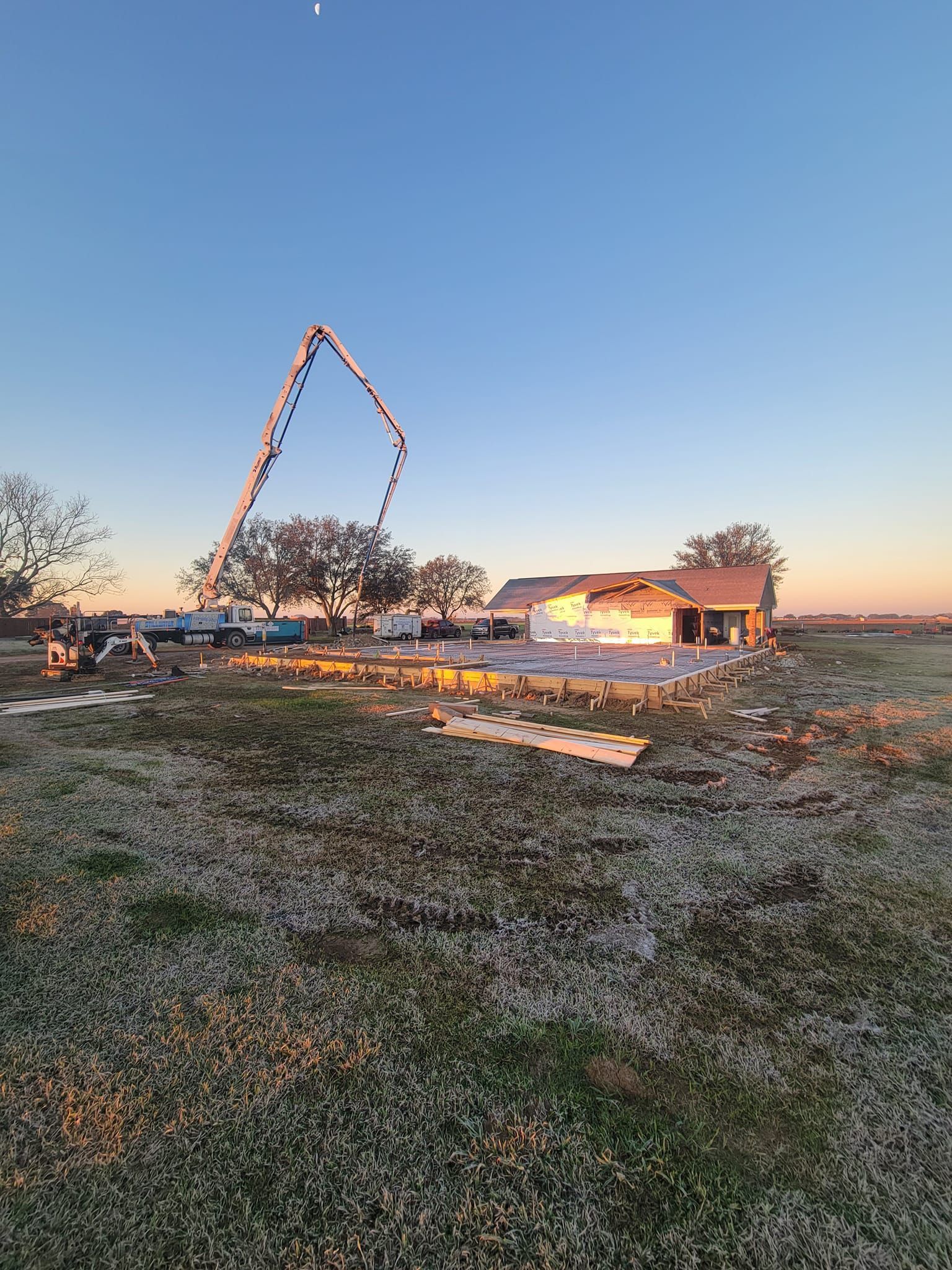 A concrete pump is being used to pour concrete in front of a house under construction.