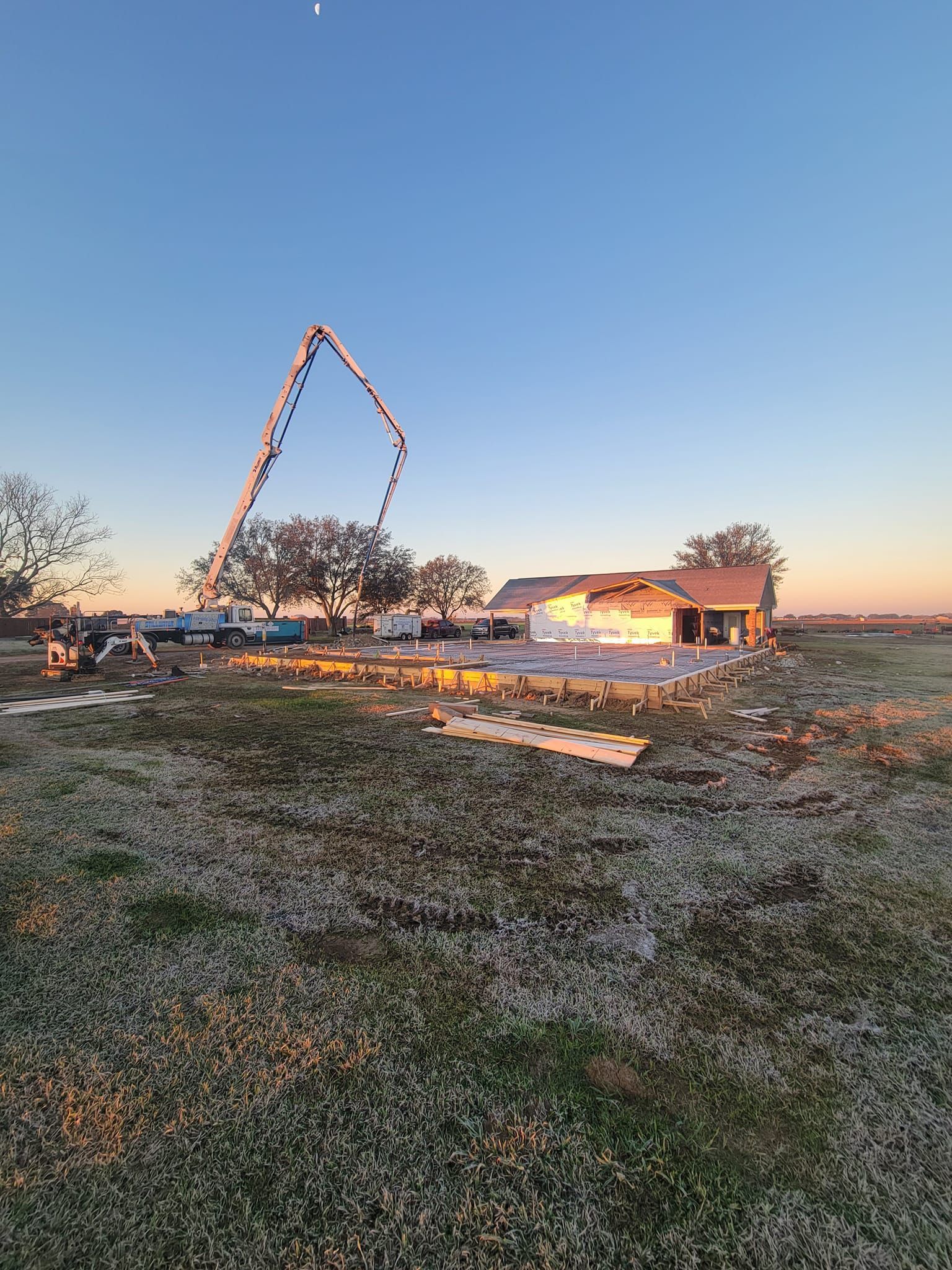 A house is being built in a field with a concrete pump in the background.