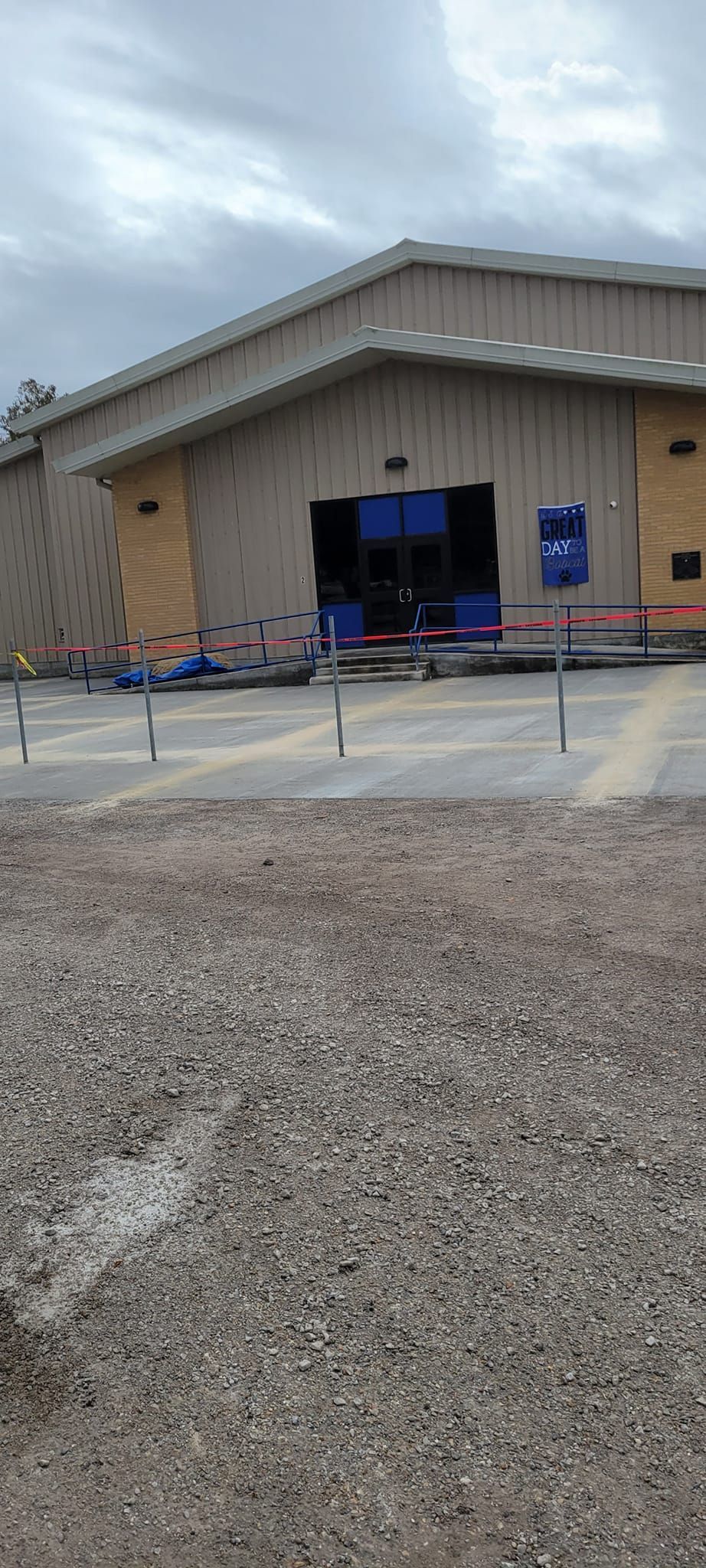 A large building with a blue door is sitting on top of a gravel lot.