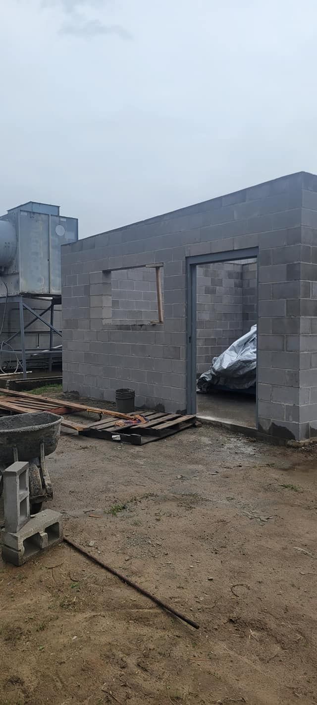 A concrete block building under construction on a cloudy day; construction materials lie around.