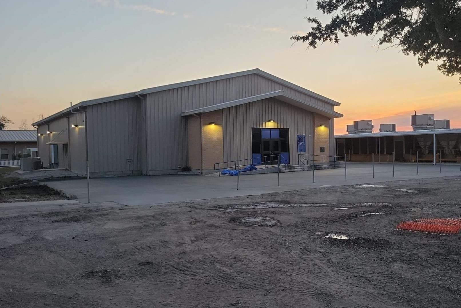 A metal building with a lit entrance and a covered walkway outside, viewed at dusk.