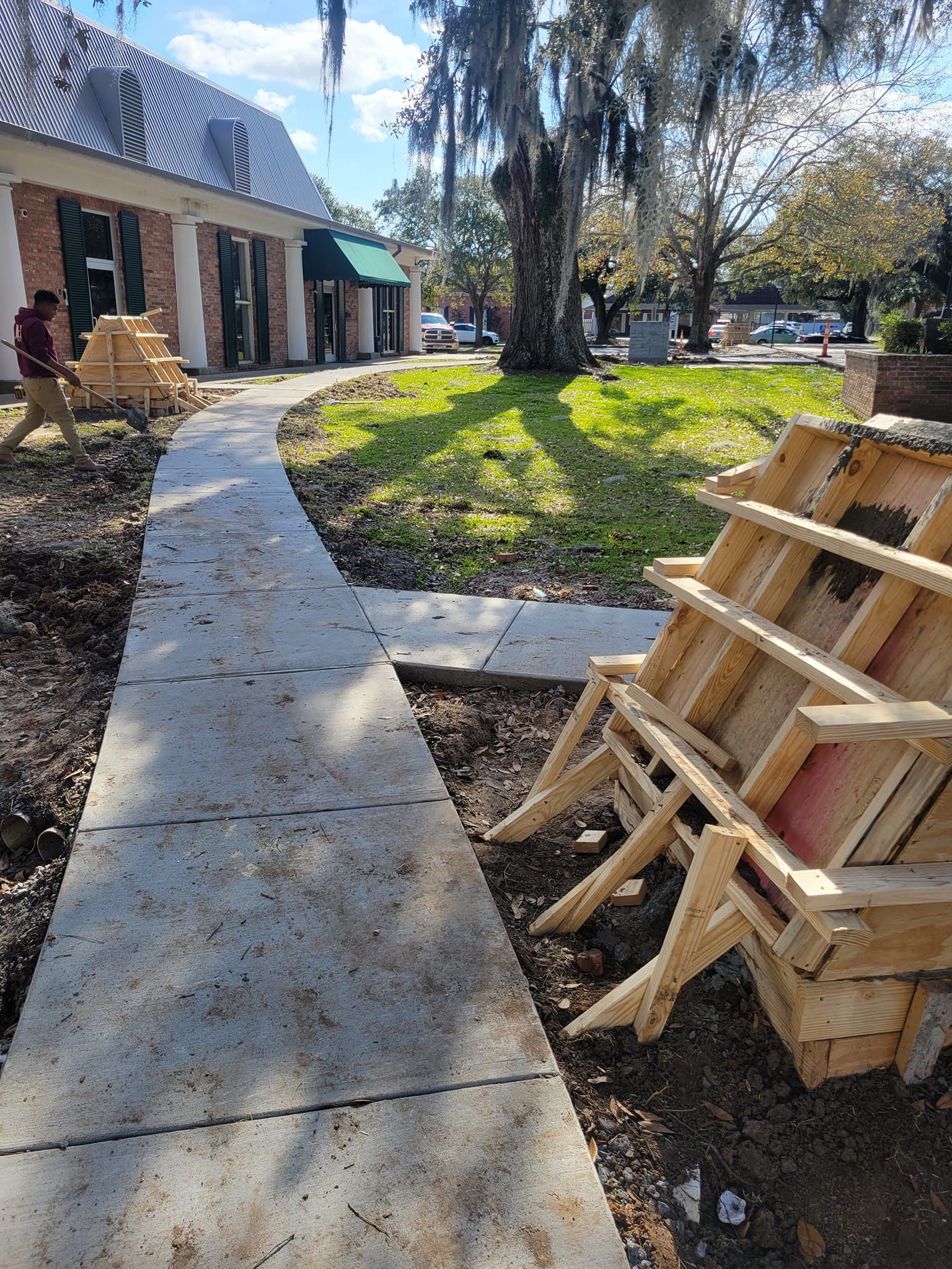 A stack of wooden chairs are sitting on the ground next to a sidewalk.