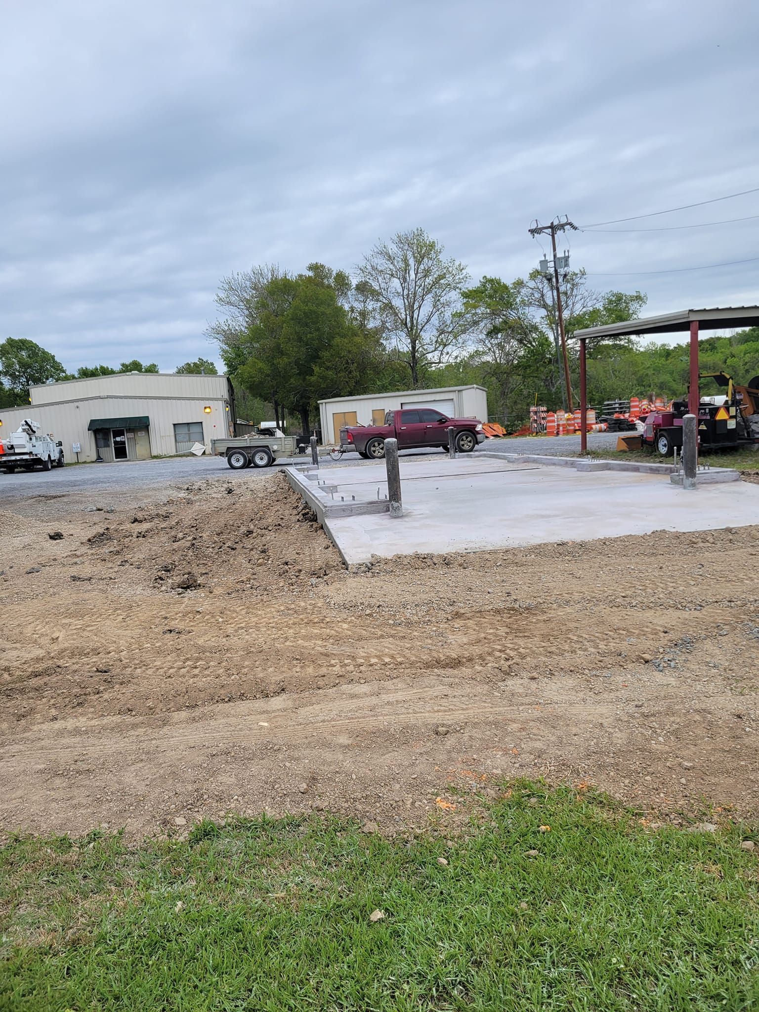A construction site with a lot of dirt and grass and a building in the background.