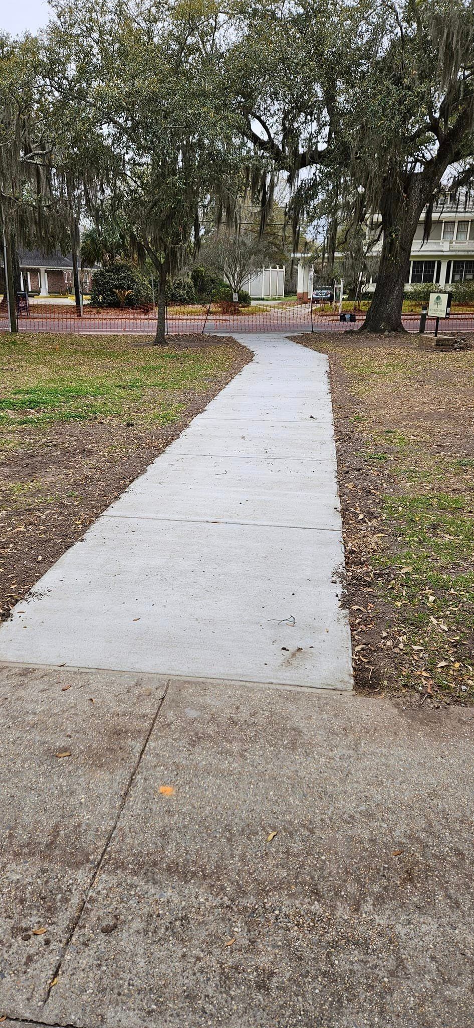 A concrete walkway in a park surrounded by trees and grass.