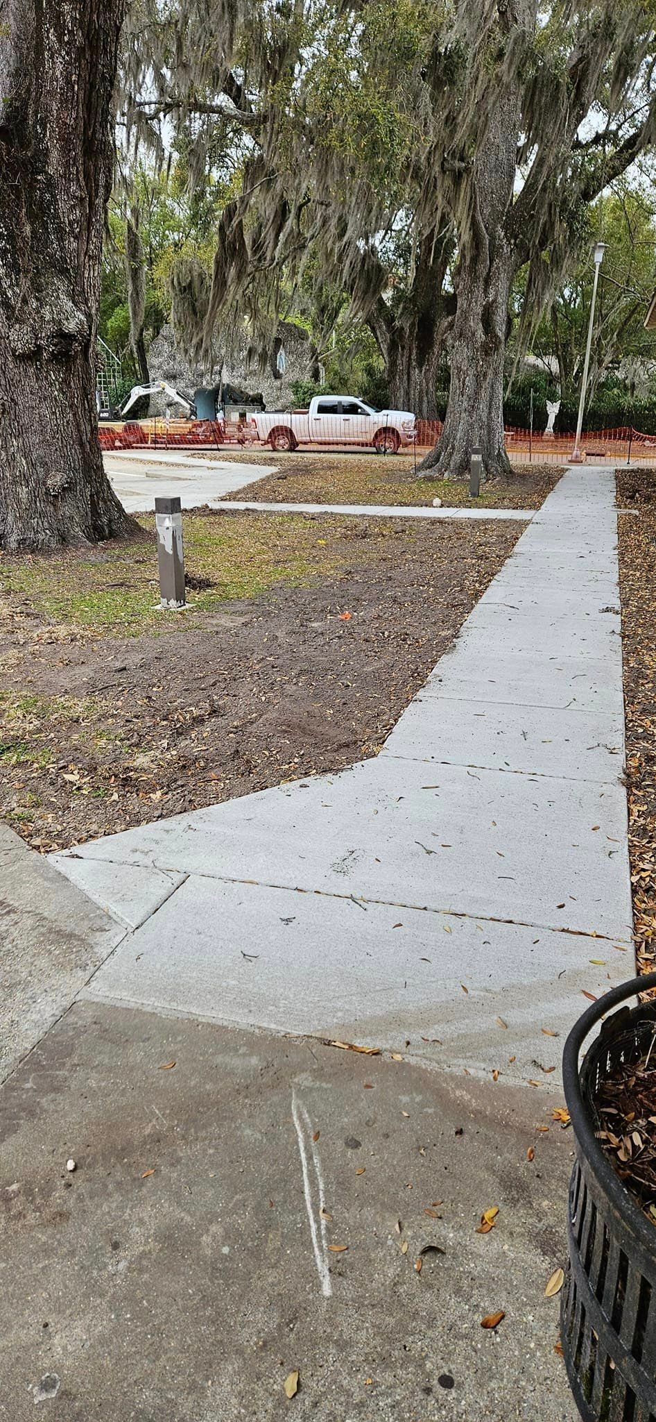 A concrete walkway with a trash can on the side of it in a park.