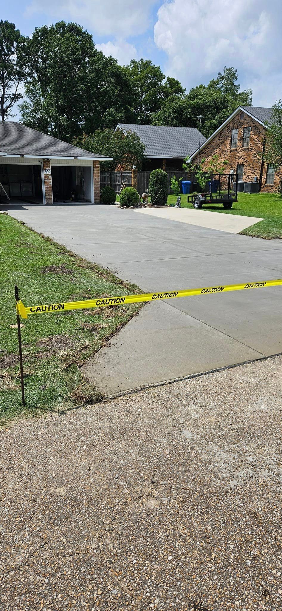 A concrete driveway with a yellow tape covering it and a house in the background.