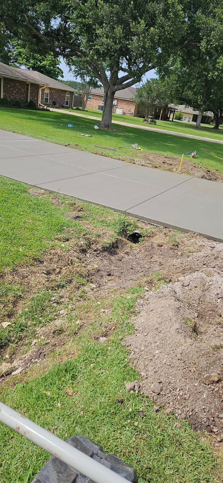 A person is using a lawn mower to cut the grass next to a sidewalk.
