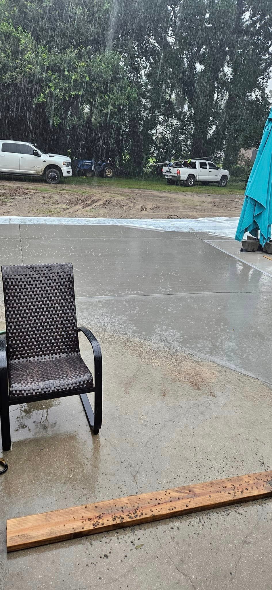 A patio with a chair , table and umbrella in the rain.