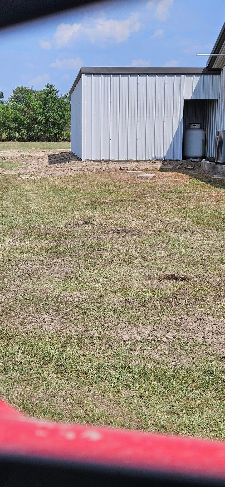 A white shed is sitting in the middle of a grassy field.