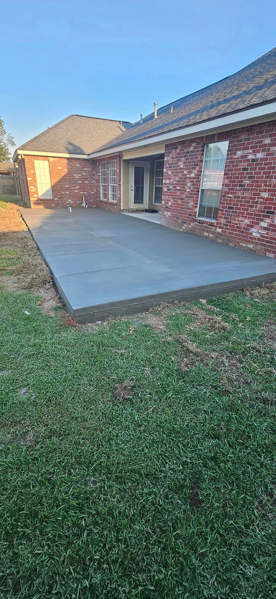 A concrete patio is being built in the backyard of a brick house.