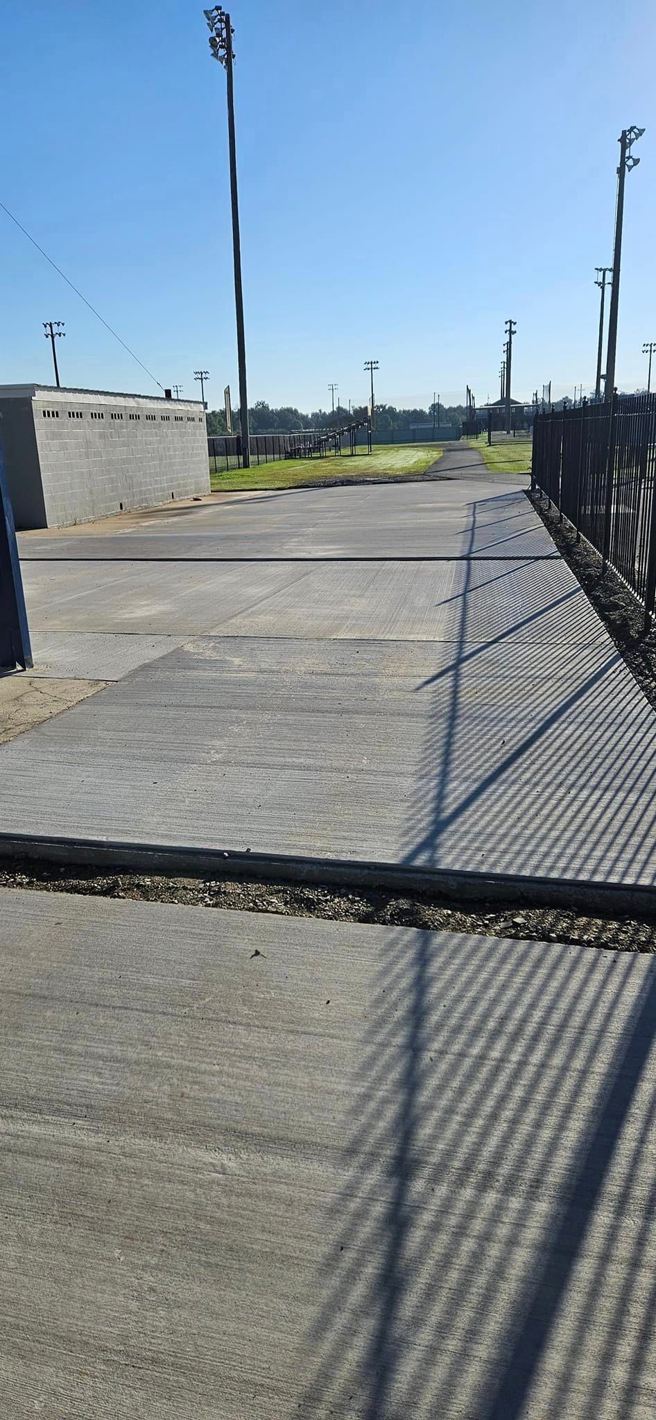 A shadow of a chain link fence is cast on a concrete walkway.