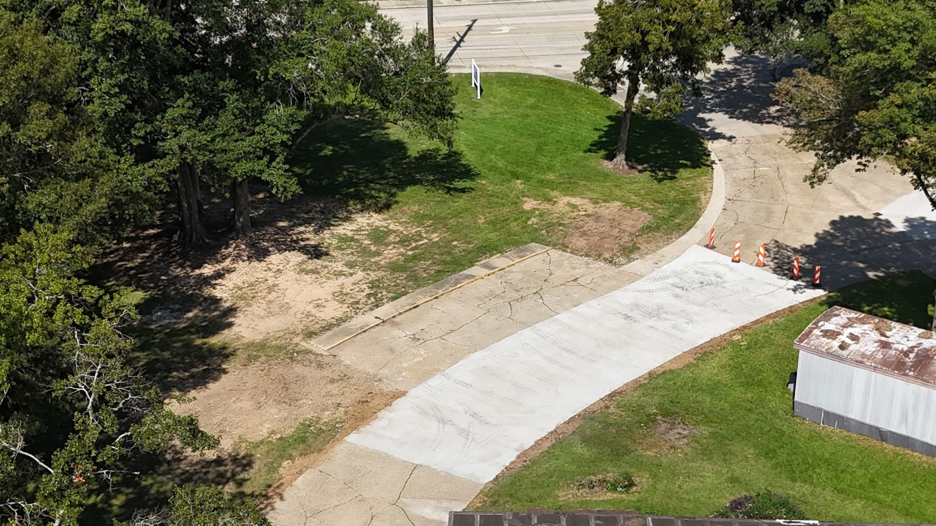 An aerial view of a concrete driveway surrounded by trees and grass.