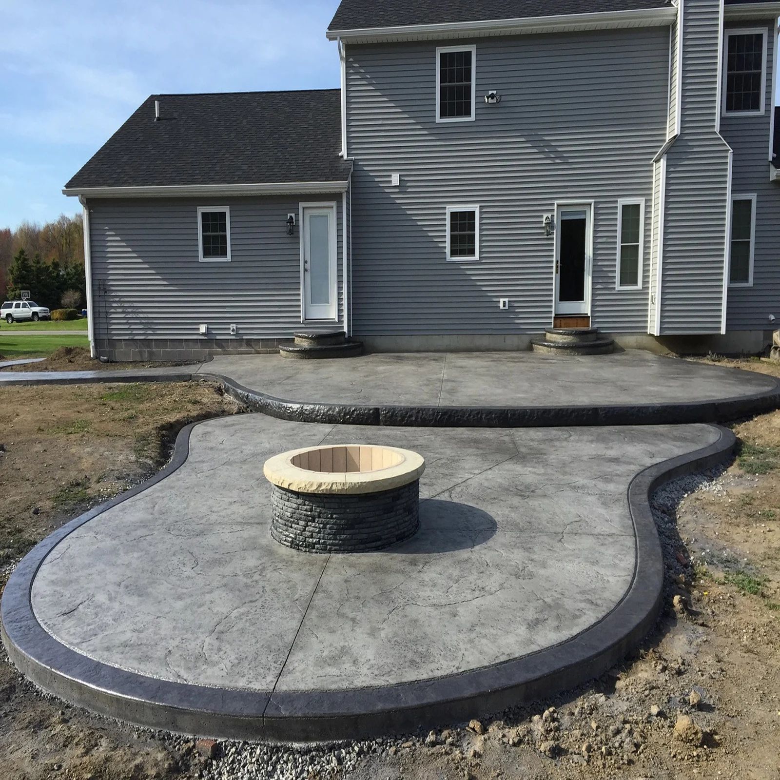 Concrete patio with fire pit in front of a two-story gray house.