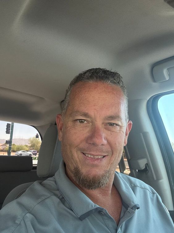 Man in car, smiling, wearing a blue shirt.