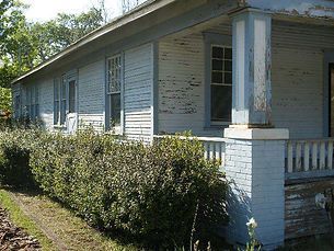 Dilapidated blue house with peeling paint and overgrown shrubs.